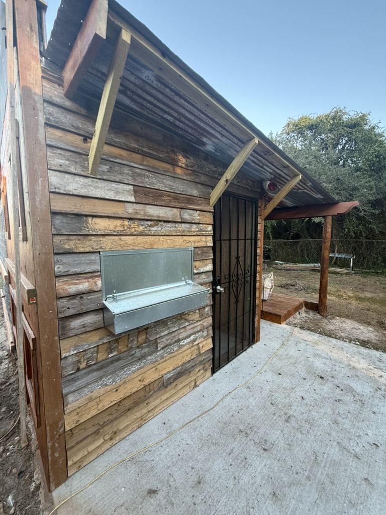 Weathered board siding with a metal feeder and an iron door on a concrete pad