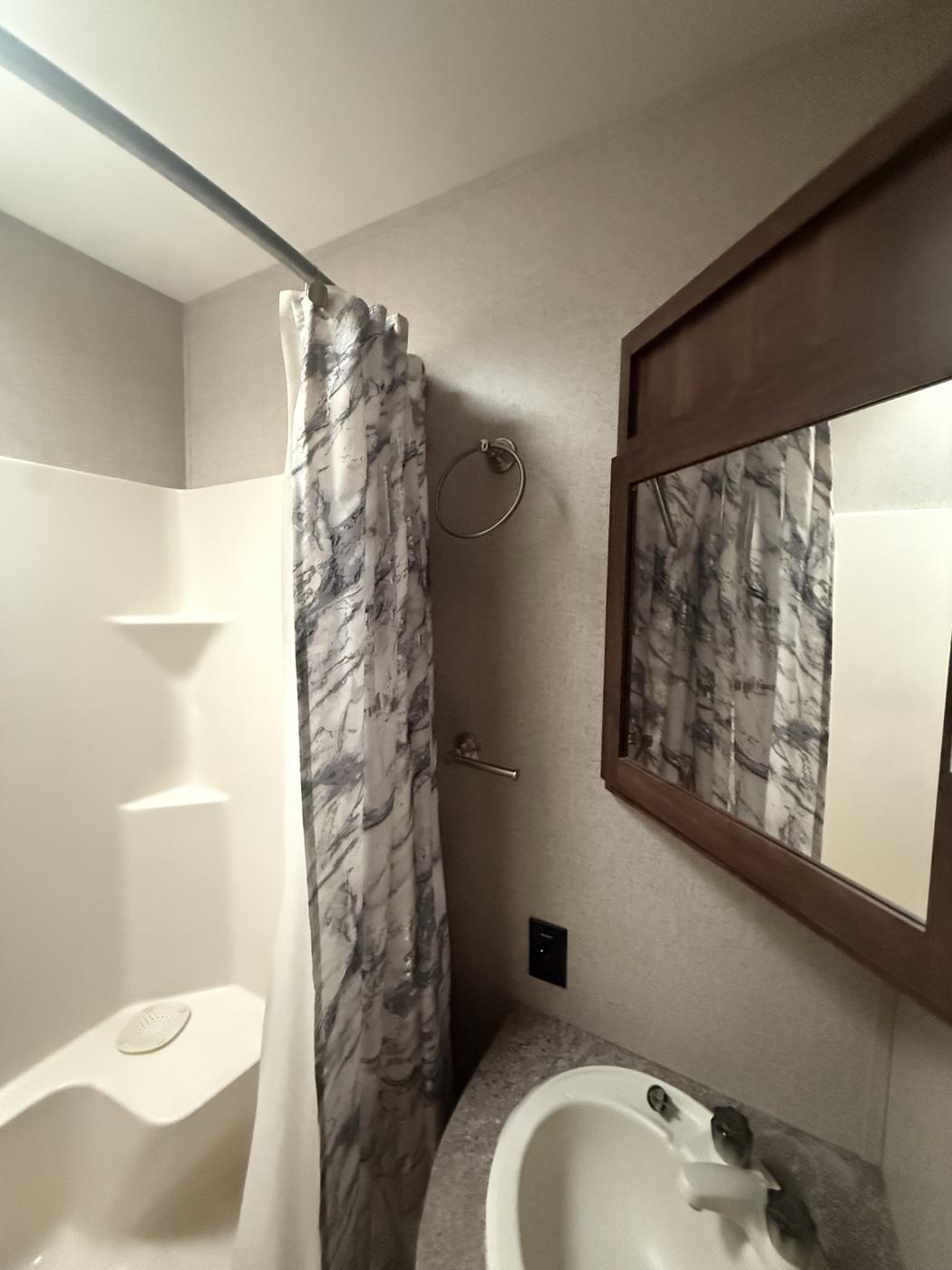 Full-size shower with curtain beside the vanity and mirror