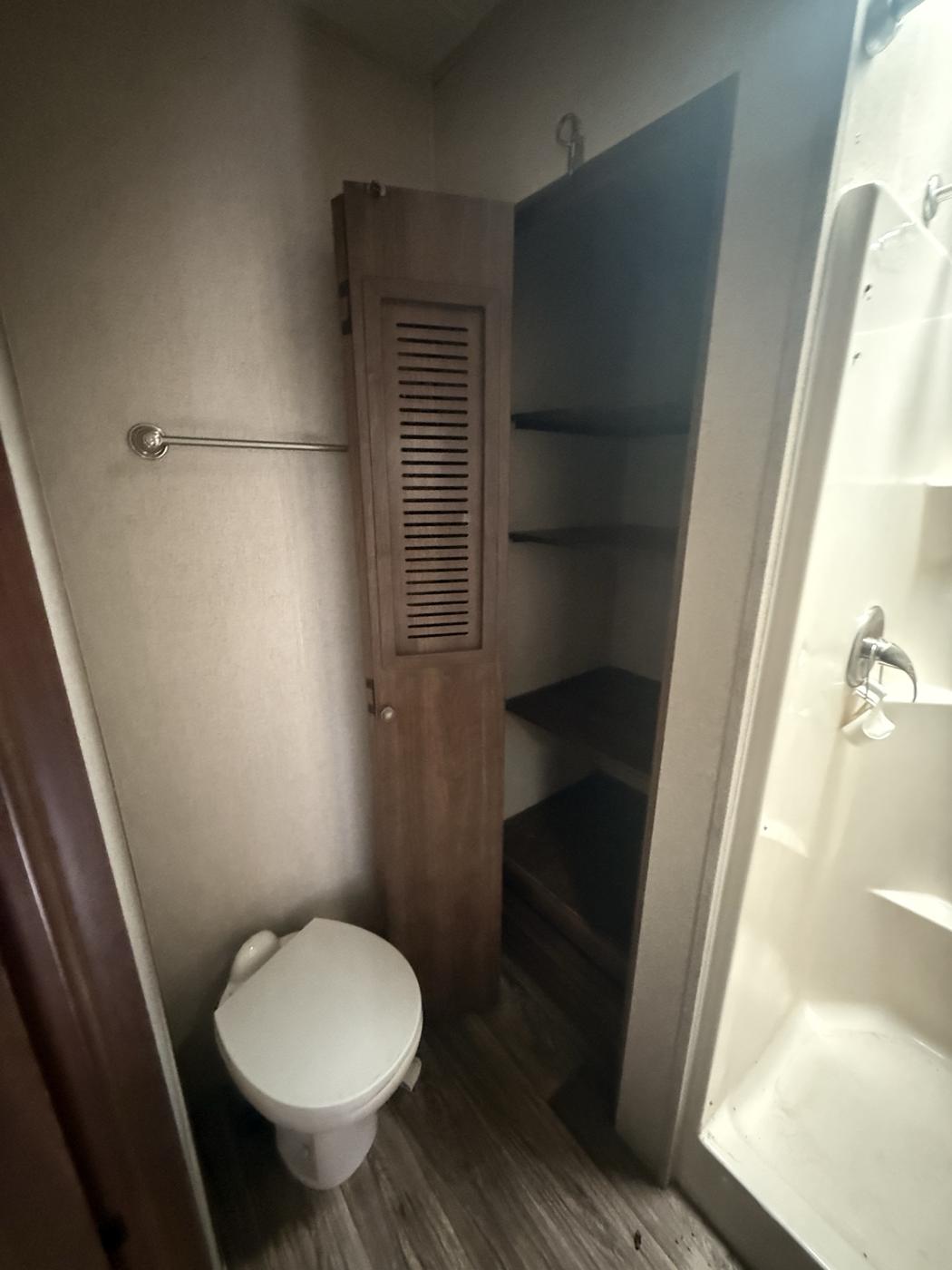 Toilet, tall linen closet with shelves, and the shower